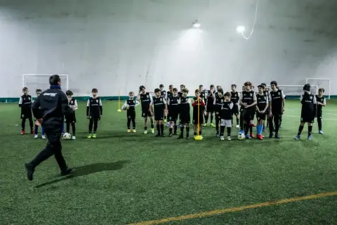 Trener prowadzi trening piłkarski metodą Coerver Coaching, instruując młodych zawodników na boisku.