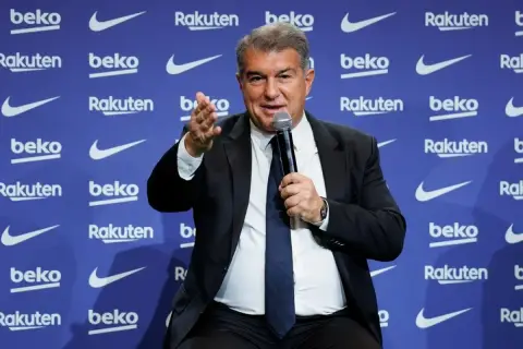 Joan Laporta, prezydent FC Barcelona, przemawia na tle logo klubu. Jego słowa kształtują przyszłość drużyny i jej trenerów.