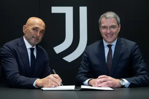 Dwóch mężczyzn w garniturach, prawdopodobnie trenerzy Juventusu, siedzi przy stole. Jeden z nich podpisuje dokumenty.